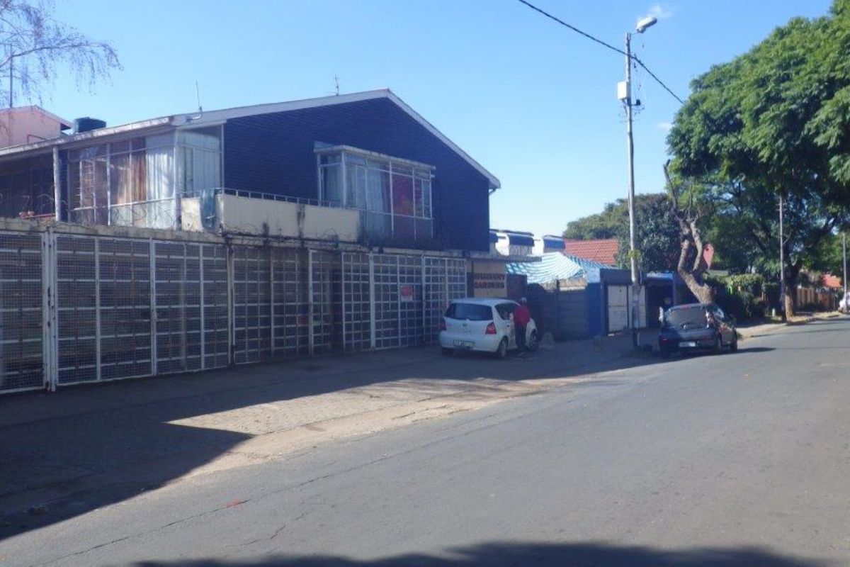 Street view of a residential flat building featuring security fencing and an upper-level balcony.