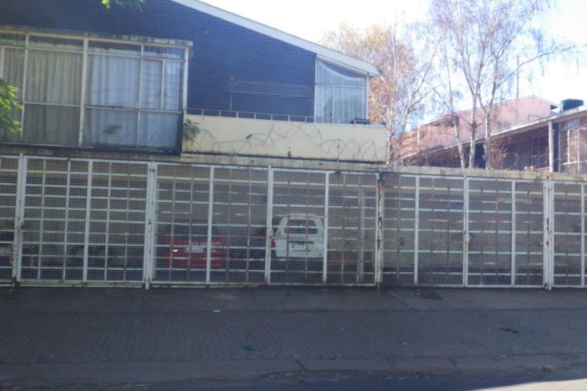Front elevation of the flat featuring a large security gate, balcony with razor wire, and visible wear on the exterior facade.