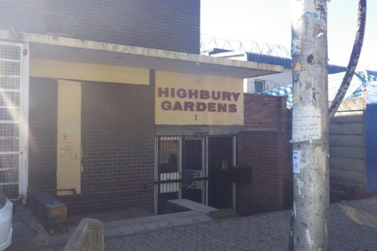 Front entrance view of Highbury Gardens apartment complex, featuring brick facade, security gate access, and perimeter razor wire fencing.