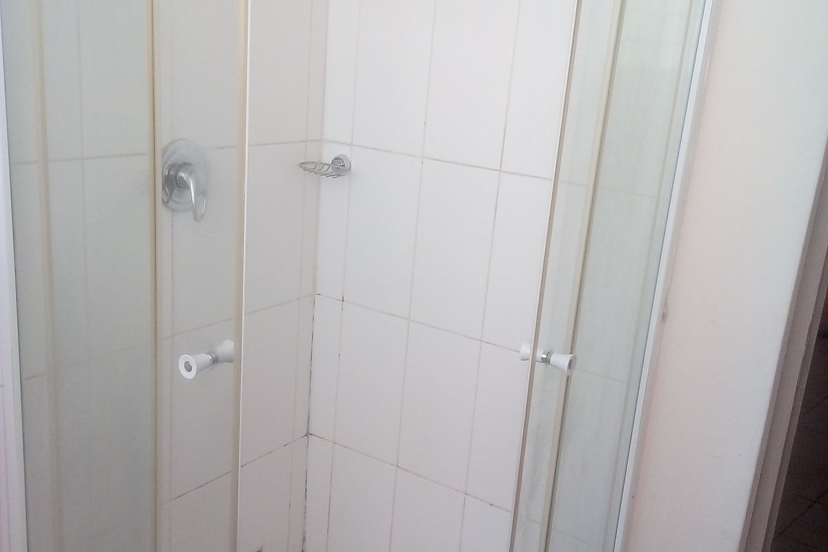 A compact shower stall featuring white wall tiles and a tiled floor, requiring maintenance to the grout and sealant.