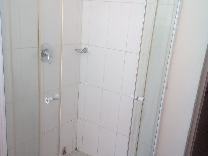 A compact shower stall featuring white wall tiles and a tiled floor, requiring maintenance to the grout and sealant.