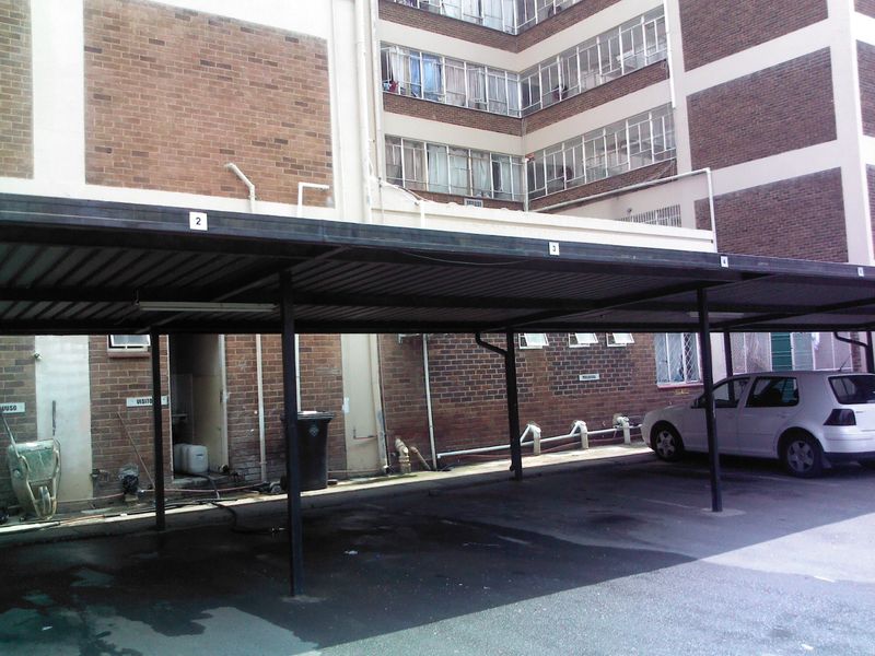 Covered carport parking area located adjacent to the main building structure with brick facade and asphalt driveway.