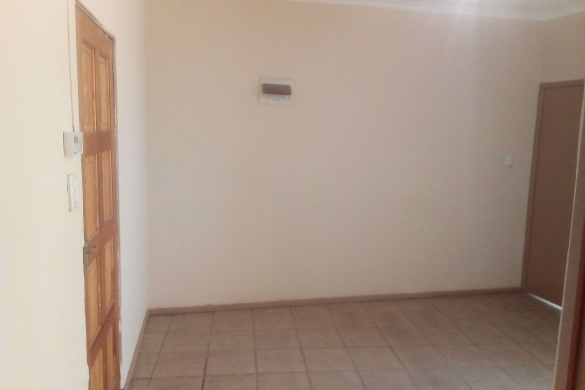 An empty, neutral-toned living area featuring tiled flooring and a wooden door, providing a blank canvas for interior design.