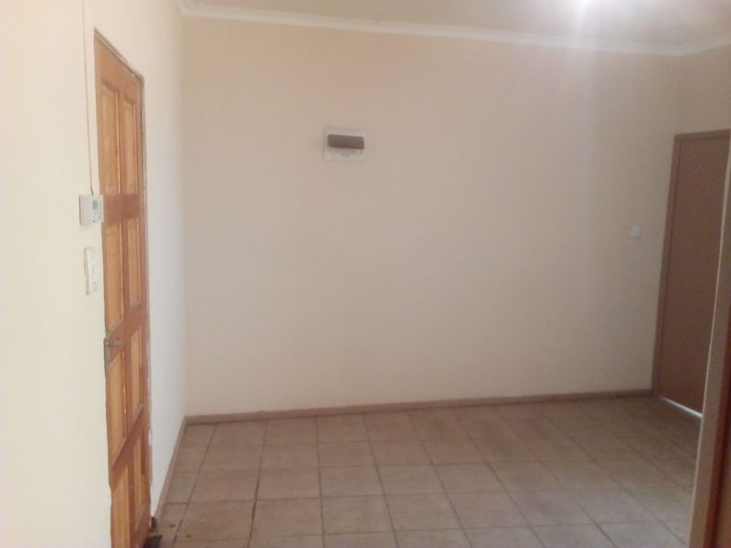 An empty, neutral-toned living area featuring tiled flooring and a wooden door, providing a blank canvas for interior design.