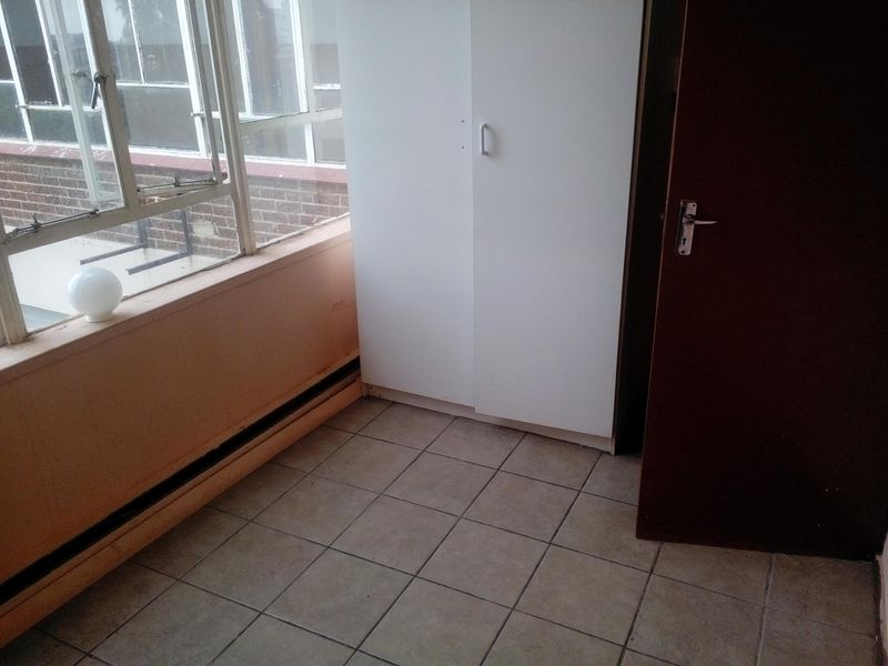 A compact bedroom featuring tiled flooring, a built-in wardrobe, and large windows providing natural light.
