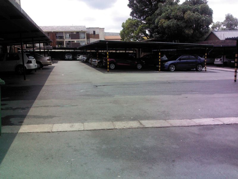 A paved outdoor parking area featuring multiple covered parking bays with steel structures for residential use.