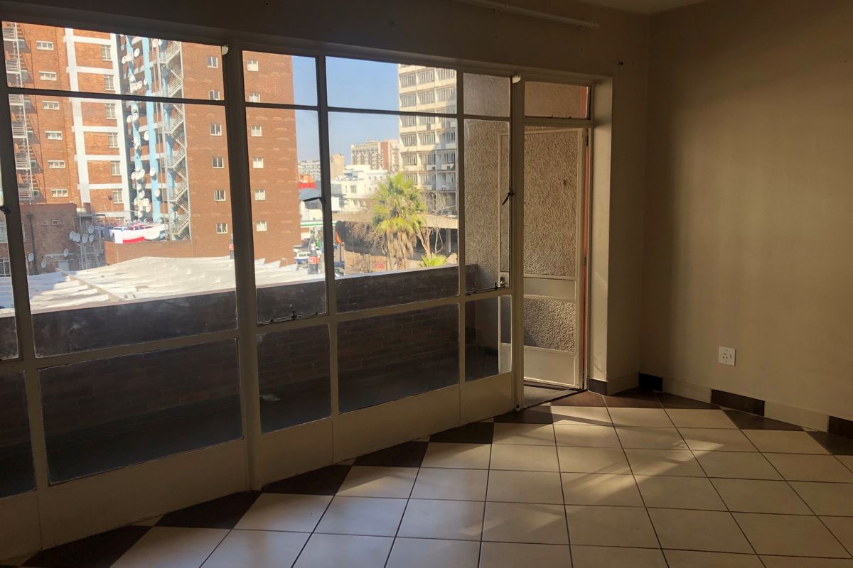 An empty living room featuring large steel-framed windows, tiled flooring, and direct access to an outdoor balcony area.
