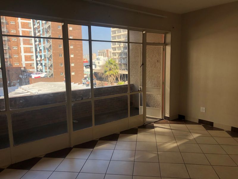 An empty living room featuring large steel-framed windows, tiled flooring, and direct access to an outdoor balcony area.