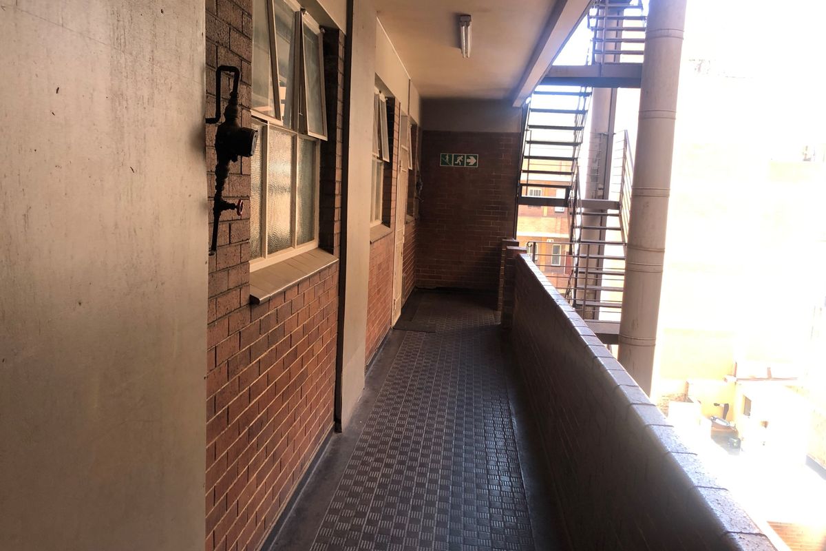 An external apartment building walkway featuring exposed brick walls, tiled flooring, and a metal fire escape staircase.