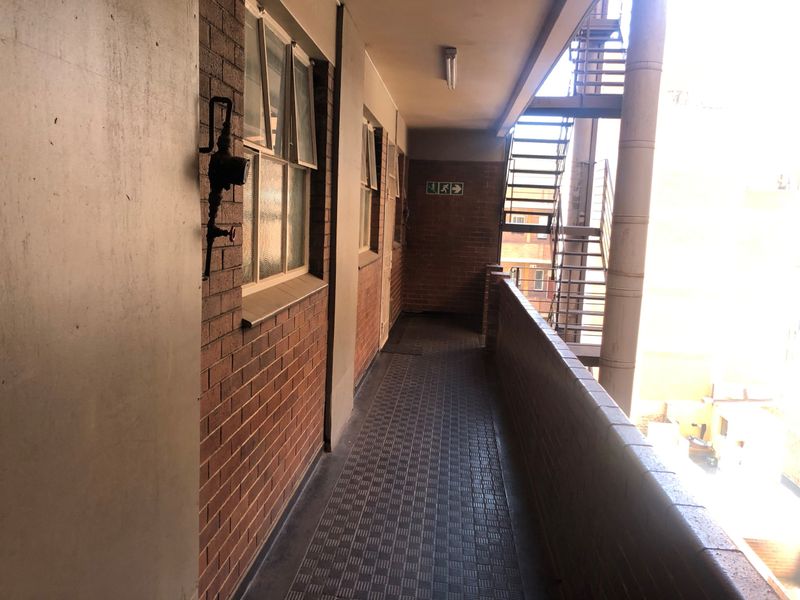 An external apartment building walkway featuring exposed brick walls, tiled flooring, and a metal fire escape staircase.
