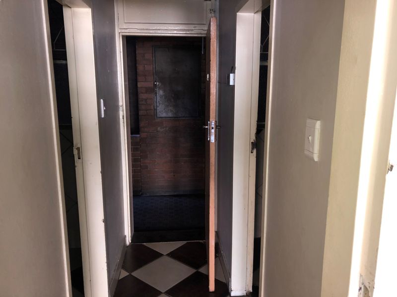 A narrow interior hallway featuring checkered floor tiles and multiple doorways leading to adjacent rooms, showing signs of wear and tear.
