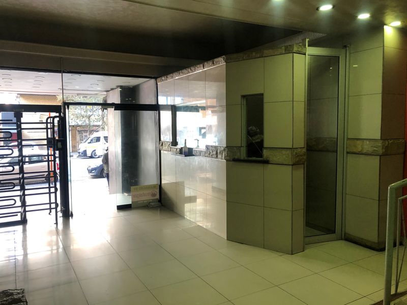 A modern building entrance lobby featuring tiled flooring, recessed lighting, a security turnstile, and a reception counter with stone cladding accents.
