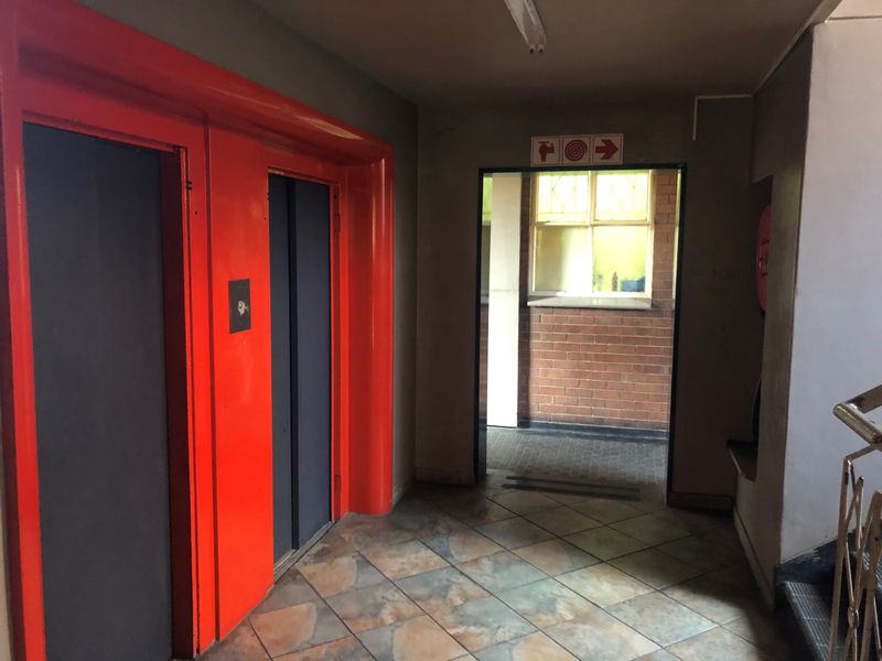 A communal hallway area featuring elevator access, tiled flooring, and a staircase, showing signs of wear and dated finishes.