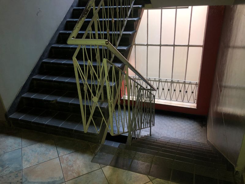 A communal stairwell area featuring tiled flooring, a metal balustrade, and a large window with security bars.