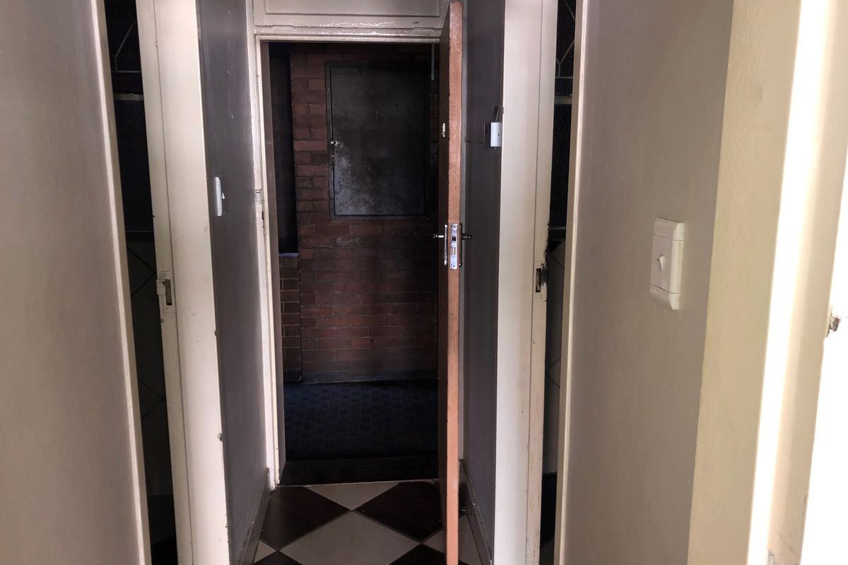 A narrow interior hallway featuring checkered floor tiles and multiple doorways leading to adjacent rooms.