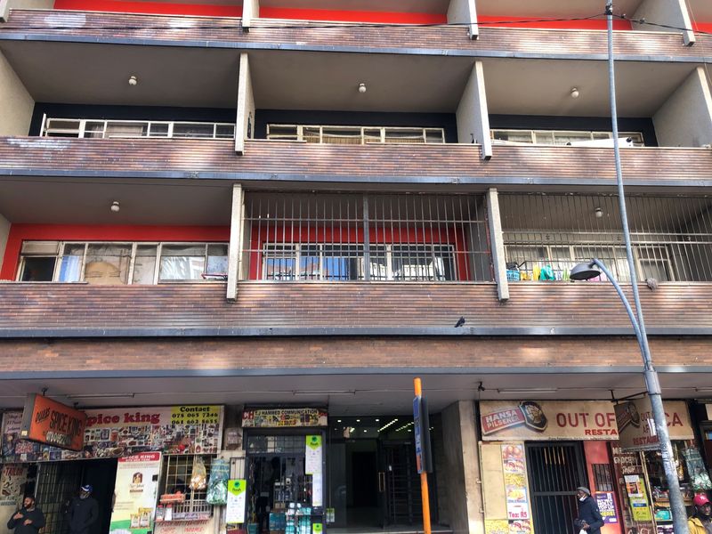 Front elevation of a multi-story apartment building featuring brick facade, balconies with security bars, and ground-level commercial retail spaces.