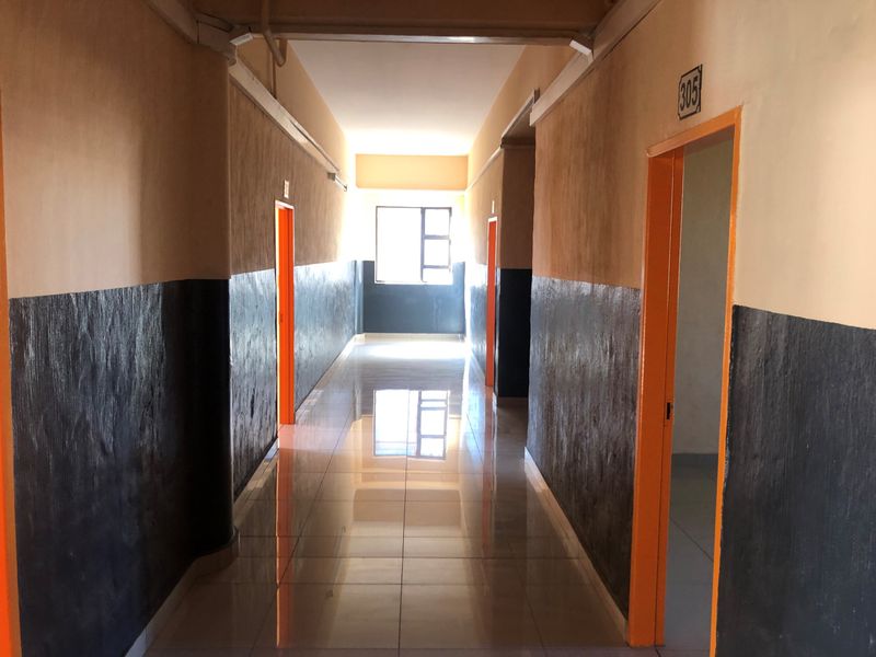 A long, empty residential hallway featuring tiled flooring and painted walls with multiple door access points.