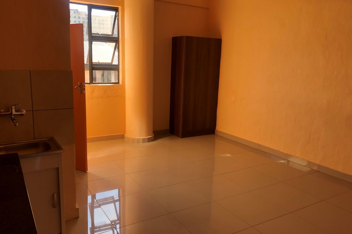 A compact, empty kitchen area featuring tiled flooring, a single sink unit, and a prominent structural column, finished with orange-toned walls.