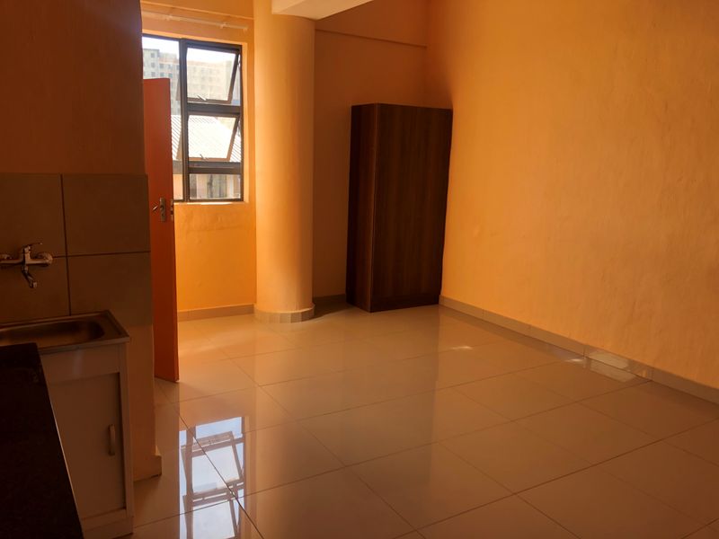 A compact, empty kitchen area featuring tiled flooring, a single sink unit, and a prominent structural column, finished with orange-toned walls.