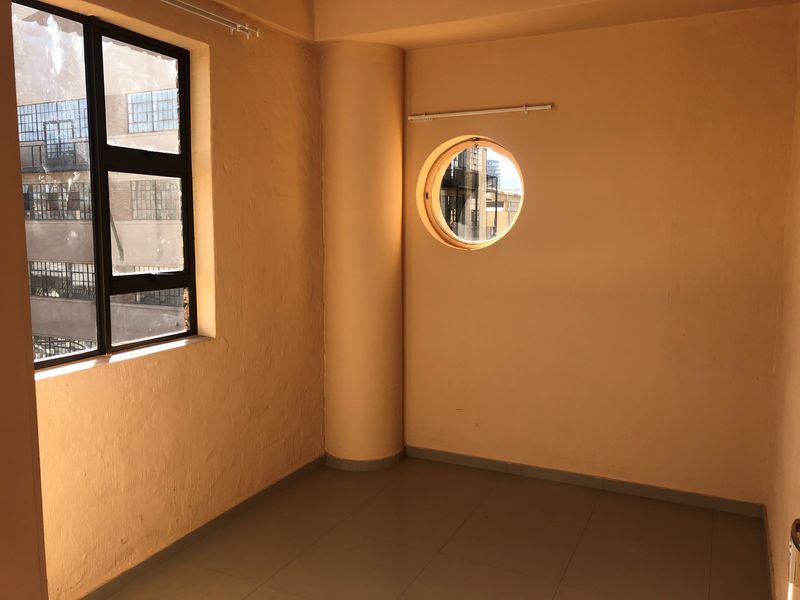 An empty bedroom featuring a unique porthole window, large rectangular window, tiled flooring, and a structural column, offering a blank canvas for interior design.
