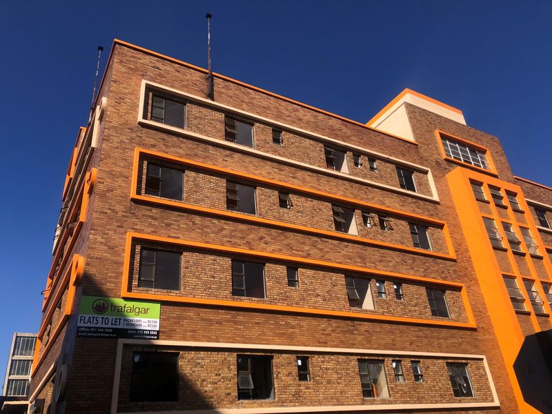 A multi-story apartment building featuring a face brick facade with orange architectural accents and numerous top-hung aluminium windows.