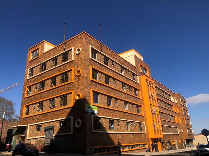 Exterior view of a multi-story brick apartment building featuring orange accents, metal window frames, and ground-level security features.