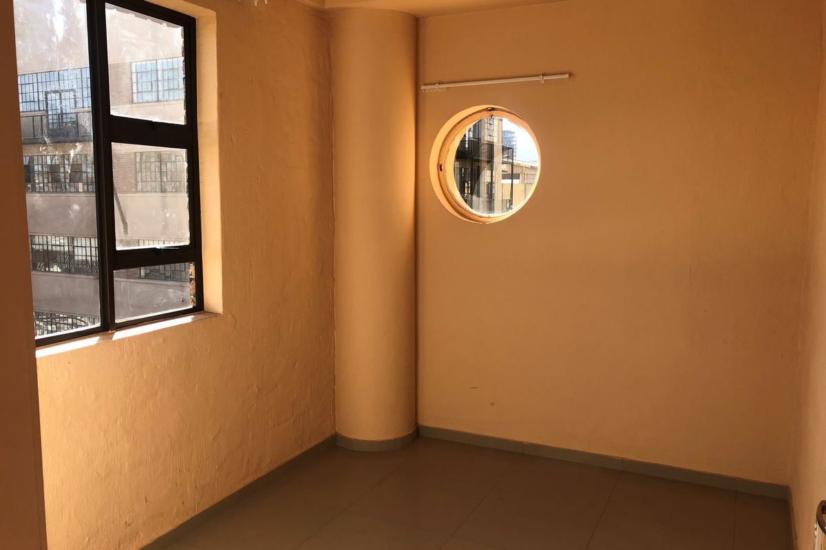 An empty bedroom featuring a unique porthole window, large rectangular window, tiled flooring, and a structural column, offering a blank canvas for interior design.