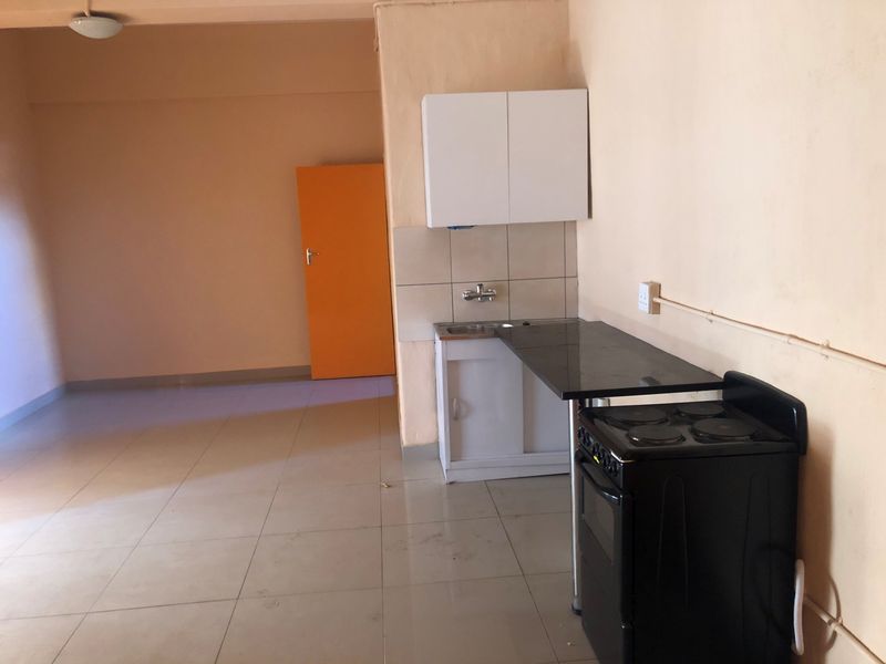 A compact, empty kitchen area featuring basic cabinetry, a sink, a tiled backsplash, and a freestanding stove, requiring cosmetic updates.