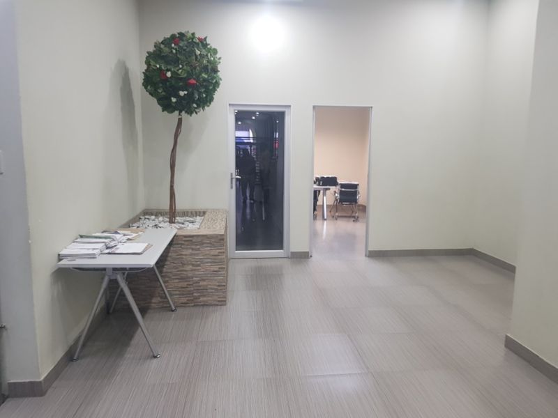 A clean, neutral hallway featuring tiled flooring, a built-in stone planter, and access to adjacent rooms through a glass panel door.