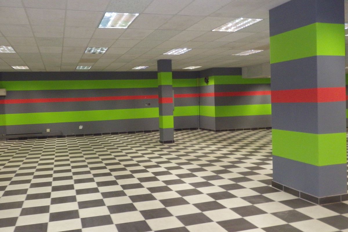 A large, open-plan commercial or utility space featuring a checkered tile floor, structural columns, and a suspended ceiling with recessed lighting.