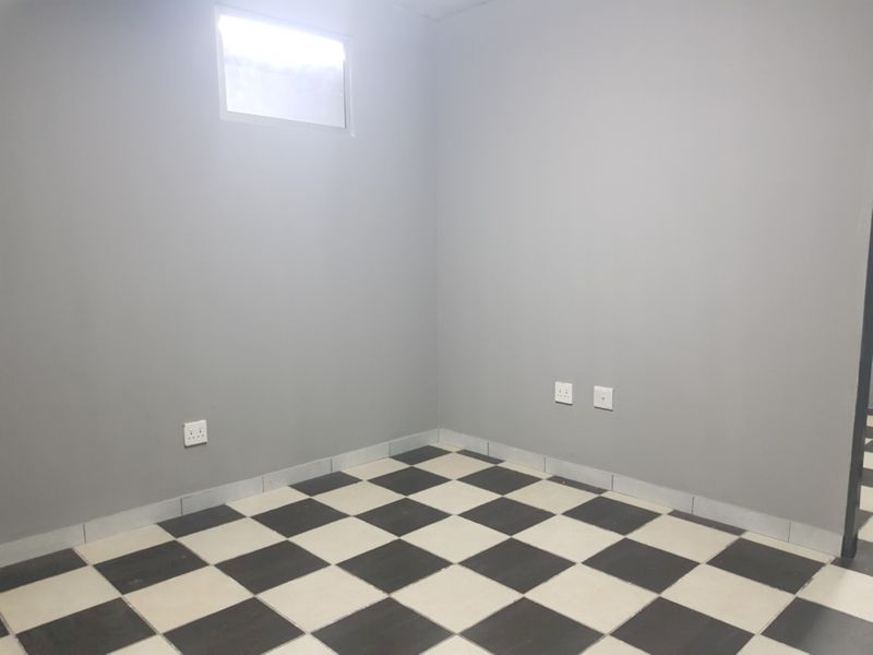 An empty bedroom featuring grey painted walls, a high-level window, and distinctive black and white checkerboard floor tiles.