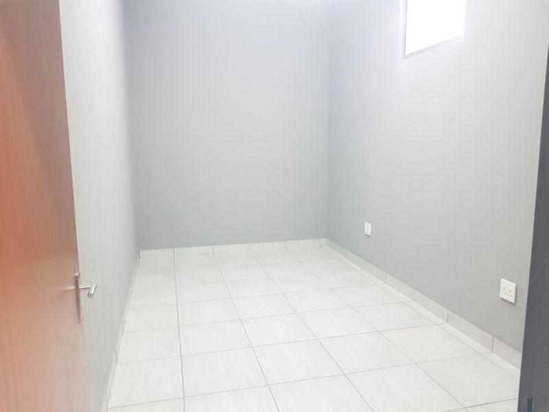 A clean, empty bedroom featuring neutral grey walls, white tiled flooring, and a high-level window, providing a versatile space ready for furnishing.