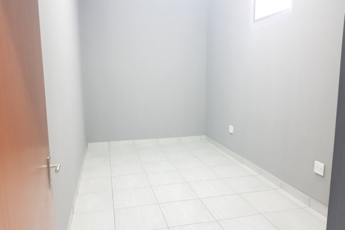 A clean, empty bedroom featuring neutral grey walls, white tiled flooring, and a high-level window for natural light.