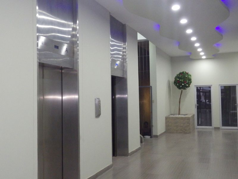 A modern apartment building hallway featuring stainless steel elevator access, tiled flooring, and decorative recessed ceiling lighting.