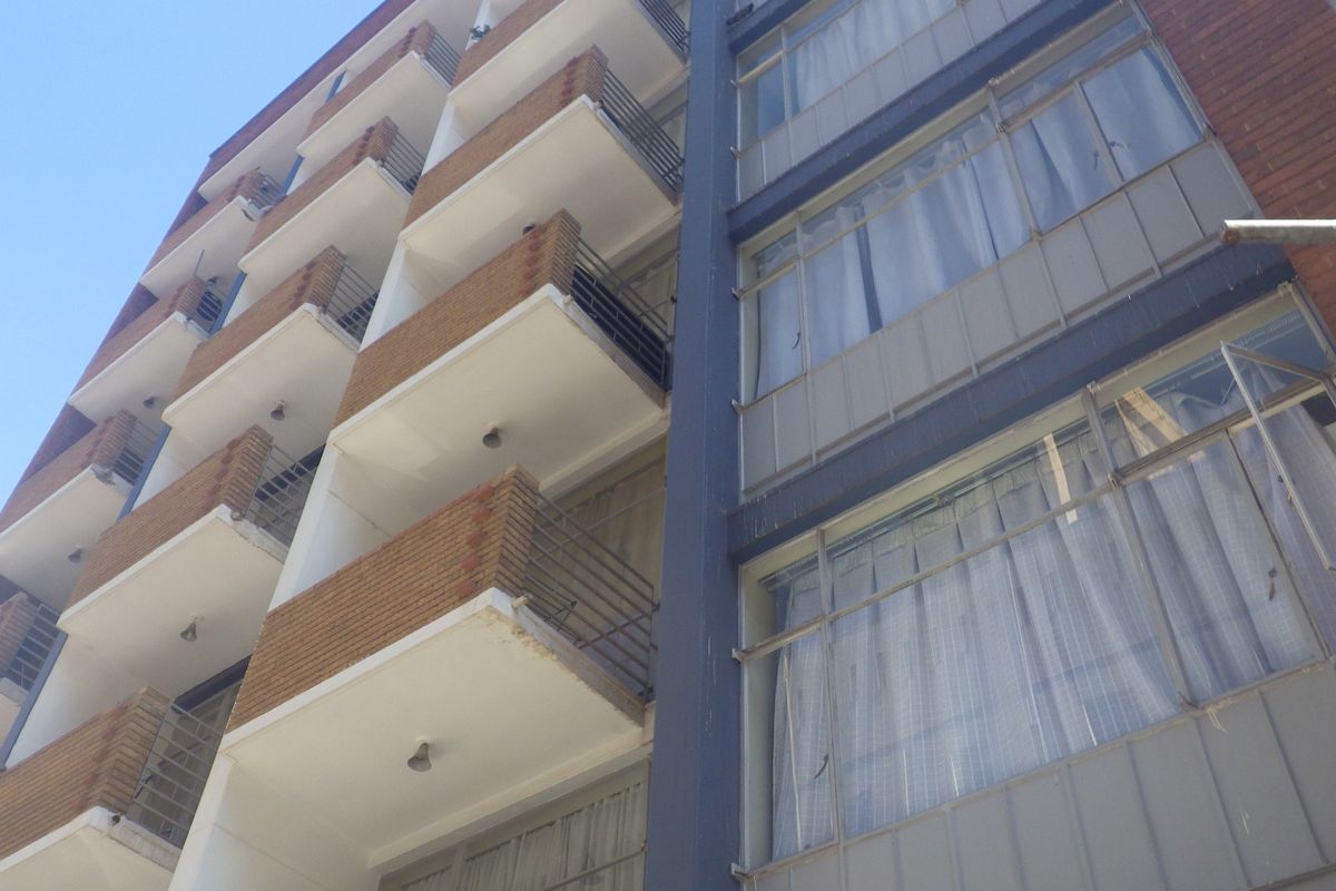 Exterior view of a multi-story apartment building featuring brick facade, private balconies with metal railings, and large windows.