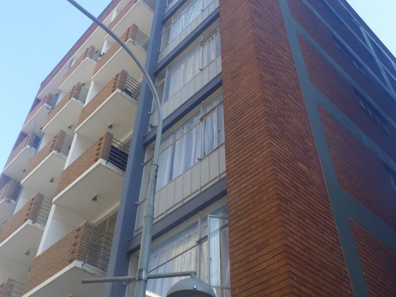 Low-angle view of a multi-story apartment building featuring a brick facade and a series of stacked balconies with metal railings.