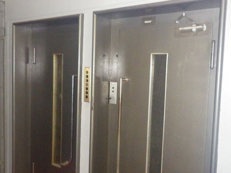 A utilitarian hallway area featuring two elevator doors with integrated call buttons and a metal security gate.