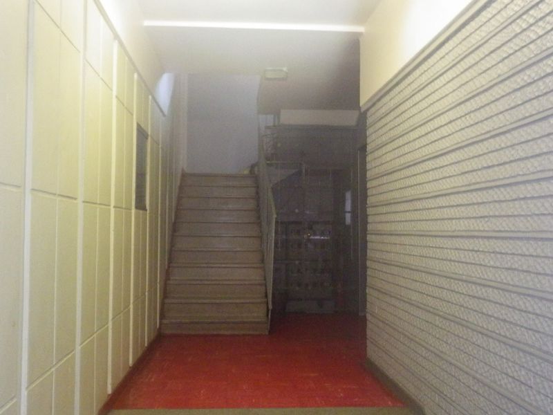 A communal hallway area featuring a staircase with a metal handrail, textured wall finishes, and tiled flooring.