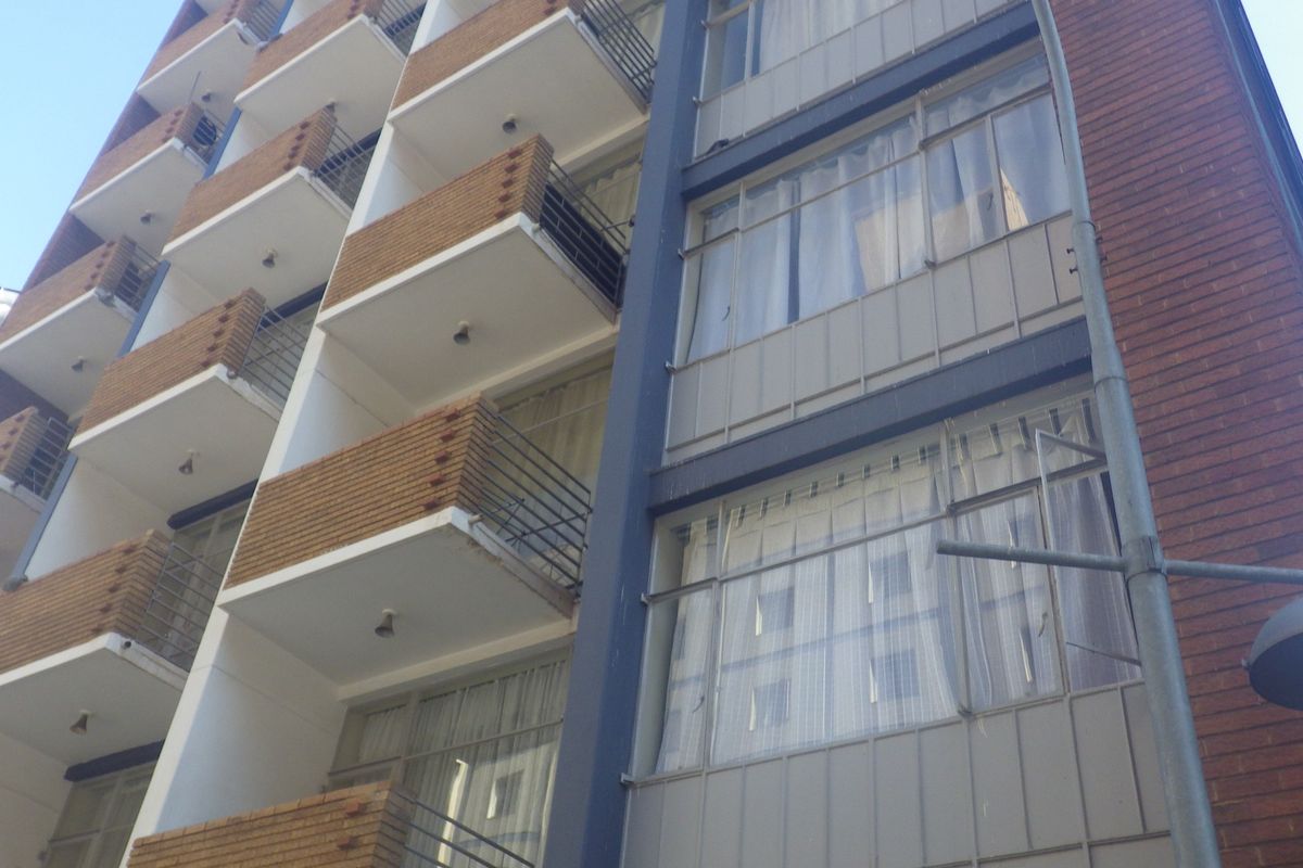 Exterior view of a multi-story apartment building featuring brick facade, private balconies with metal railings, and large windows.