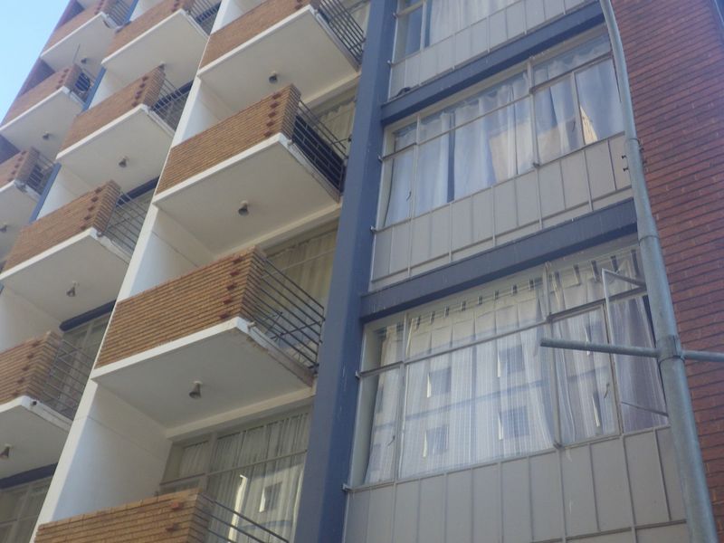 Exterior view of a multi-story apartment building featuring brick facade, private balconies with metal railings, and large windows.