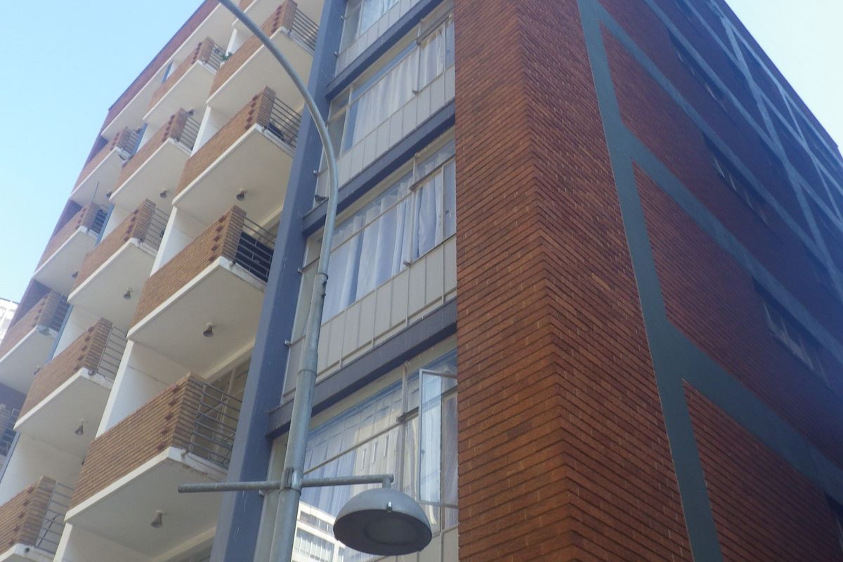 A low-angle view of a multi-story apartment building featuring a brick facade and a series of private balconies with metal railings.