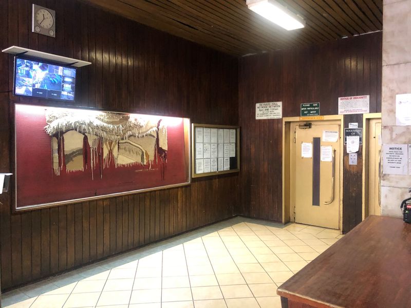 Building entrance lobby featuring wood-paneled walls, tiled flooring, a reception counter, and elevator access with security signage.