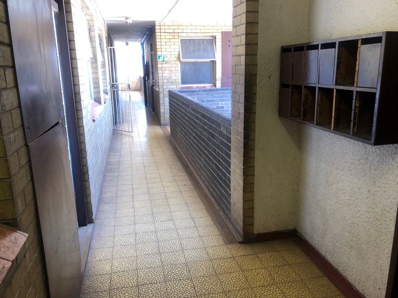 A communal apartment hallway featuring brick wall finishes, tiled flooring, and built-in mailboxes, showing signs of age and wear.