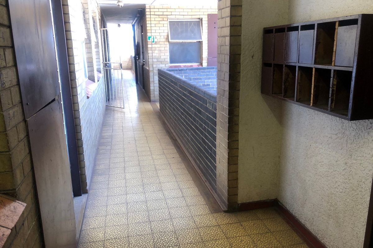 A communal apartment hallway featuring brick wall finishes, tiled flooring, and built-in mailboxes, showing signs of age and wear.