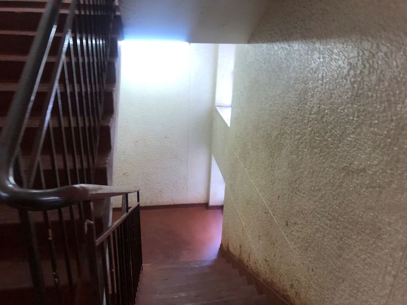 A communal stairwell featuring a metal balustrade and textured walls, showing signs of wear and requiring maintenance or cosmetic updates.
