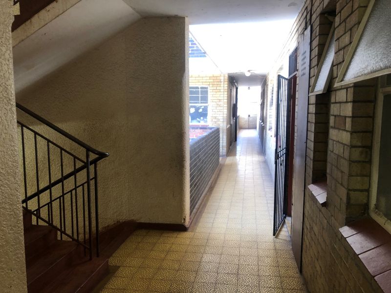 An exterior-facing communal hallway featuring brick walls, tiled flooring, and a metal staircase with a security gate.