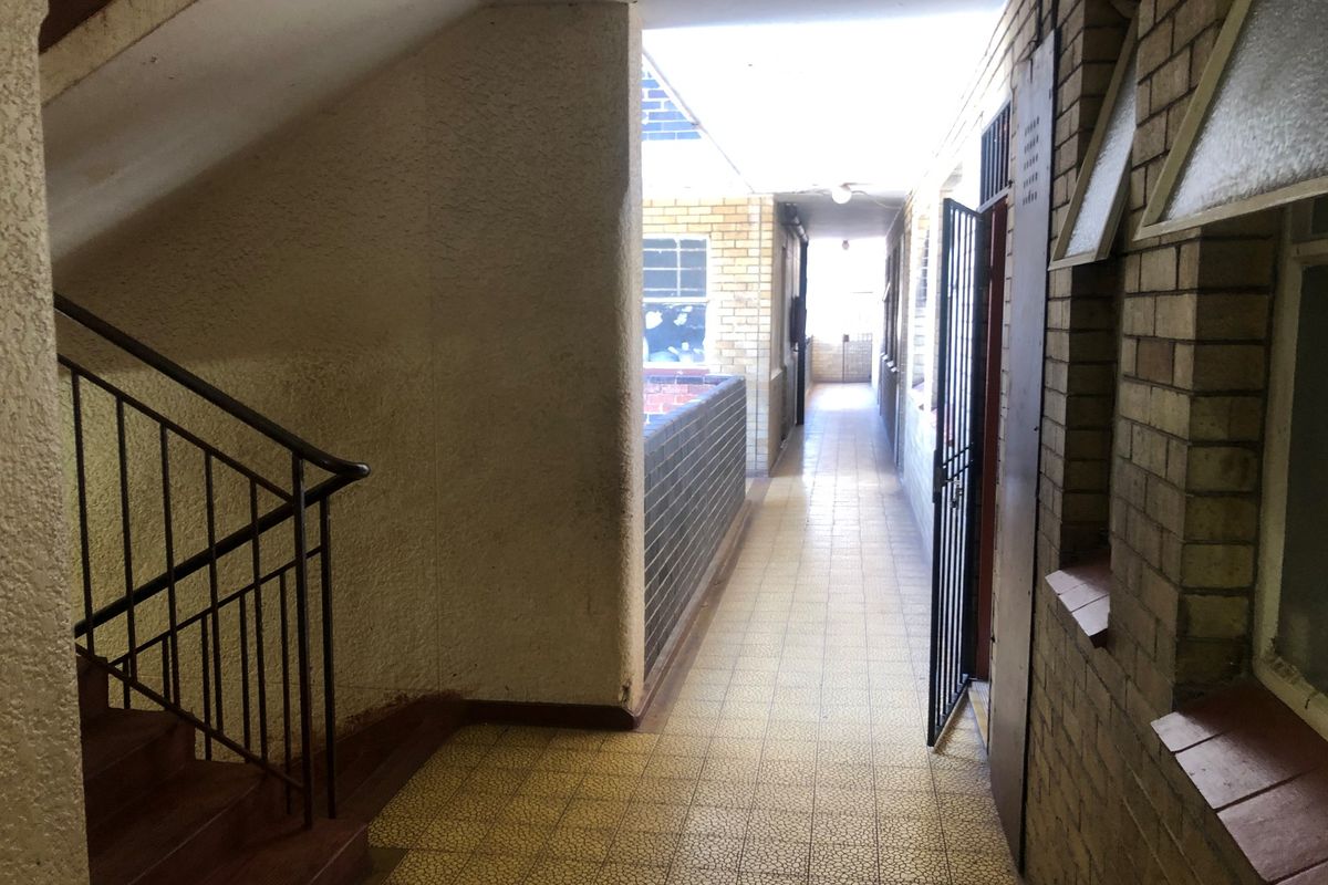 An exterior-facing communal hallway featuring brick walls, tiled flooring, and a metal staircase with a security gate.
