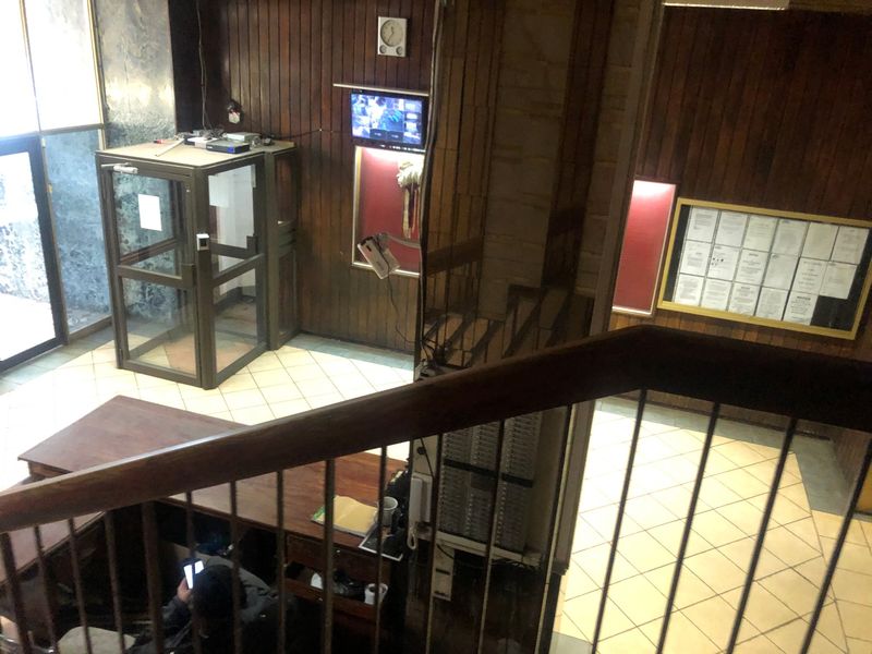 Entrance lobby area featuring wood paneling, tiled flooring, a security booth, and a notice board, viewed from an elevated staircase position.