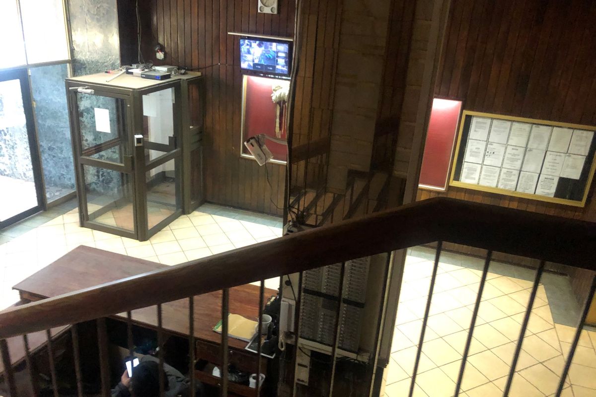 Entrance lobby area featuring wood paneling, tiled flooring, a security booth, and a notice board, viewed from an elevated staircase position.