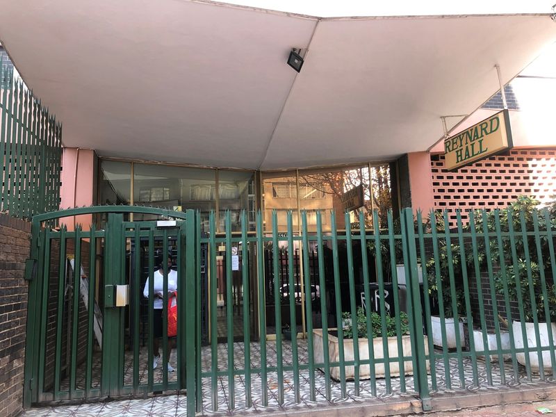 Front entrance of Reynard Hall featuring a secure metal gate, covered canopy, and brick facade with glass entrance doors.
